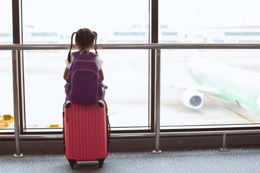 Cute asian child girl with backpack looking at plane and waiting for boarding in the airport